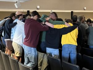 a dozen young men in a semi-circle praying